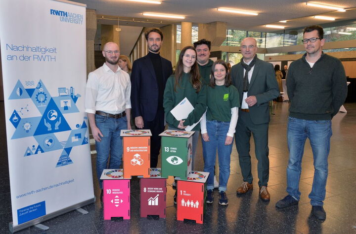 Sieben Personen schauen in die Kamera, im Vordergrund stehen fünf Hocker in den Farben verschiedener nachhaltiger Entwicklungsziele der Vereinten Nationen.