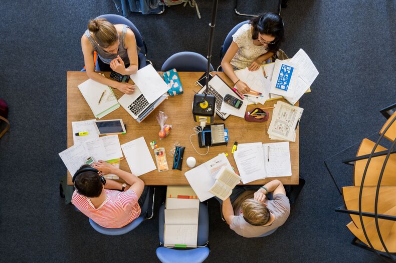 Zwei weibliche und zwei männliche Personen sitzen an einem Tisch. Sicht von oben. Auf dem Tisch sind Lernmaterialien ausgebreitet.