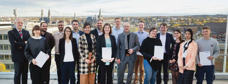 17 Menschen, darunter Rektor Rüdiger und die vertreter*innen der geförderten Projekte, lächeln in die Kamera. Im Hintergrund befinden sich die Aachener Innenstadt mit Dom und Rathaus.