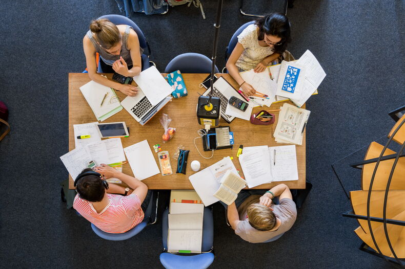 Two females and two males sitting at a table. View from above. Learning materials are spread out on the table.