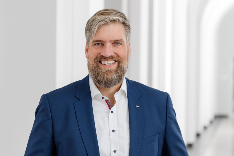Professor Kai-Uwe Schröder, Vorsitzender des Senats der RWTH Aachen, blickt in die Kamera und lacht. Er trägt einen blauen Anzug und ein weißes Hemd.